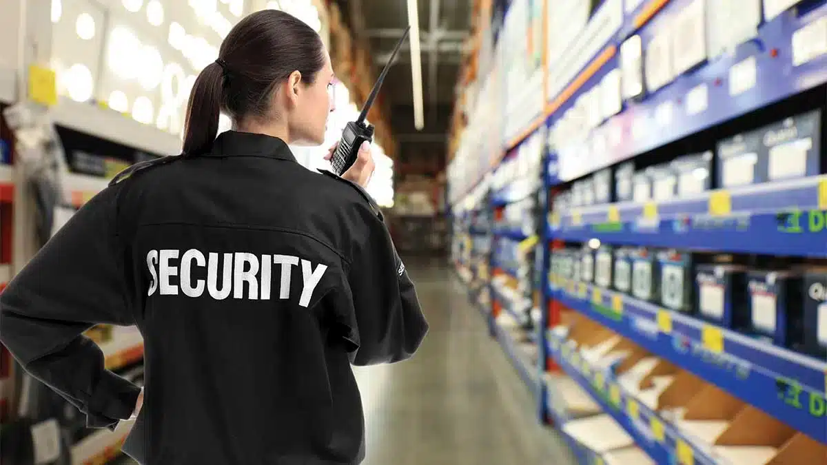 Warehouse-Security-Services-in-Dallas-image Security guard patrolling warehouse aisle with radio.